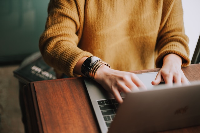 Woman in brown sweater writing on a laptop